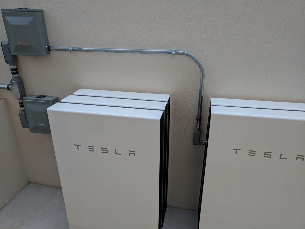 duży biały magazyn energii obok paneli słonecznych na zielonej trawie